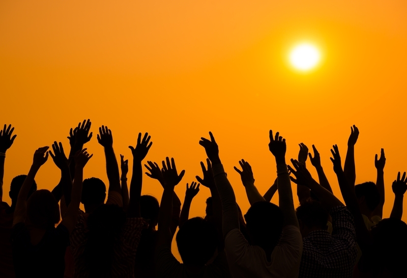 Crowd with raised hands silhoutted against orange sky and sun