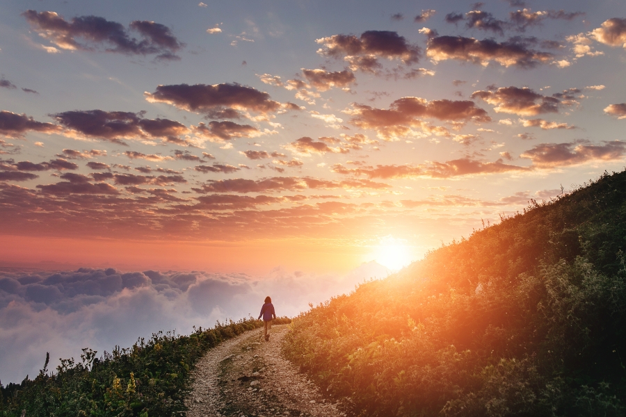 woman walking on curving path on mountain at sunrise